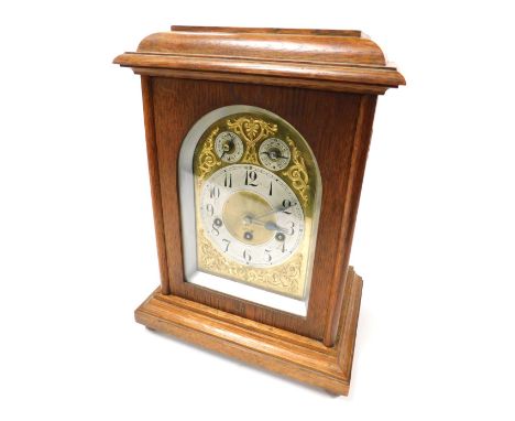 An early 20thC oak cased mantel clock, domed brass dial with foliate spandrels, circular silver chapter ring bearing Arabic n