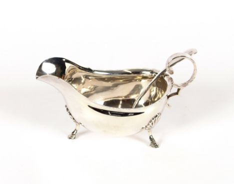 A George V silver sauce boat, having serrated border, flying C scroll handle raised on three shell decorated hoof feet; and a