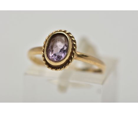 A 9CT GOLD AMETHYST SINGLE STONE RING, the oval cut amethyst within a collet setting, to the rope twist surround and plain ba