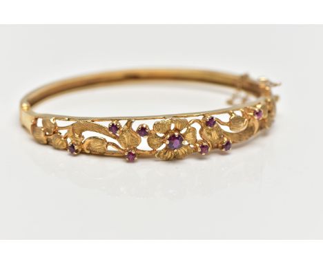 A 9CT GOLD FLORAL BANGLE, a yellow gold oval form hinged bangle, open work textured detail set with nine circular cut garnet 