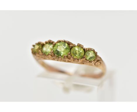 A 9CT GOLD FIVE STONE PERIDOT RING, designed with five graduated circular cut peridots, scrolling gallery and shoulders leadi