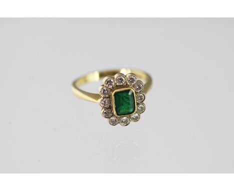 An emerald and diamond cluster ring, the central rectangular emerald within a surround of twelve brilliant cut diamonds, all 