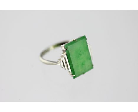 A jade set ring, the rectangular panel set within stepped white metal shoulders, to the tapering shoulders and plain hoop sta