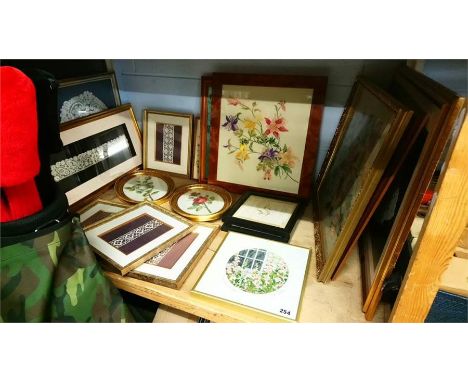 A shelf of embroidered and needlework pictures.