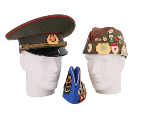 A Soviet army peaked cap together with two caps having numerous badges affixed