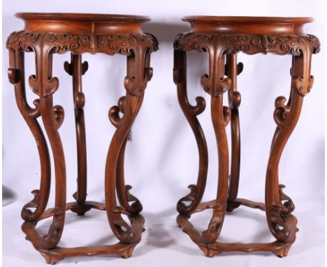 A pair of Chinese hardwood jardiniere stands with inset walnut circular panel to the top, carved scroll apron raised on scrol