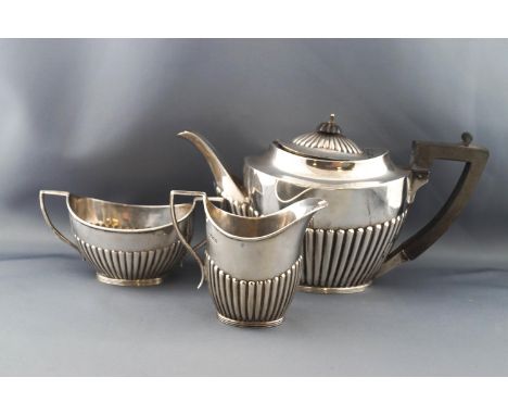 A silver oval part fluted three piece tea service in Queen Anne style, the teapot with an ebonised handle and finial, London 