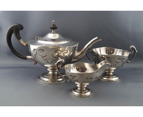 A silver round pedestal three piece tea service, each with gothic cut-card decoration, leaf scroll handles on a round pedesta