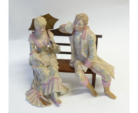 PAIR OF 19th CENTURY TINTED BISQUE FIGURES modelled as a gallant and his companion seated on a wooden bench, unmarked, 11 1/2
