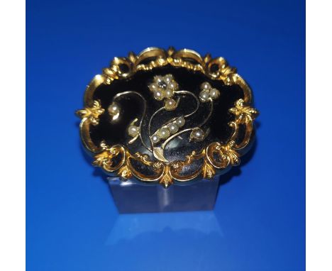 A Victorian oval mourning brooch with gilt scroll border and central seed pearl flowers against a black enamel ground, monogr
