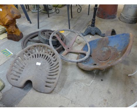 Two vintage cast iron tractor seats, a steering wheel and two cast iron wheels 