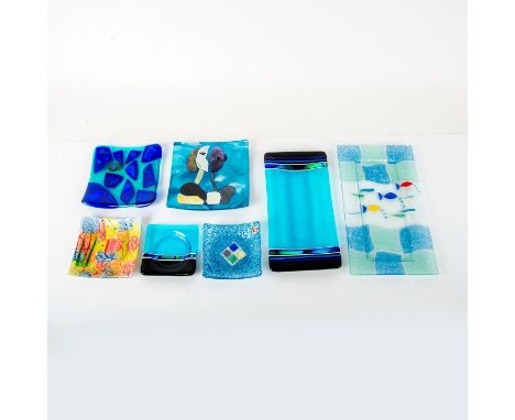 A set of seven plates of various designs, sizes, and patterns. 1) A small blue and black square plate with a circular indent.