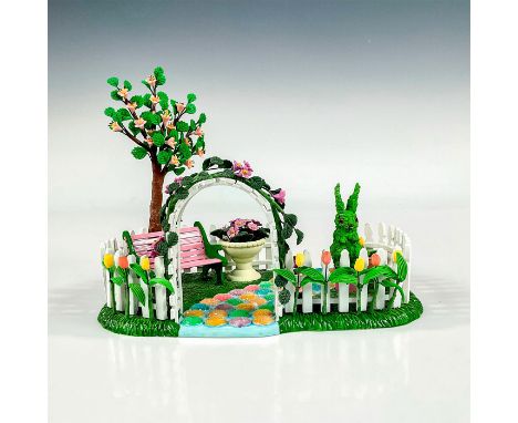 The Original Snow Village series; a ceramic figure of a yard adorned with a white picket fence, tulips, potted flowers, and g