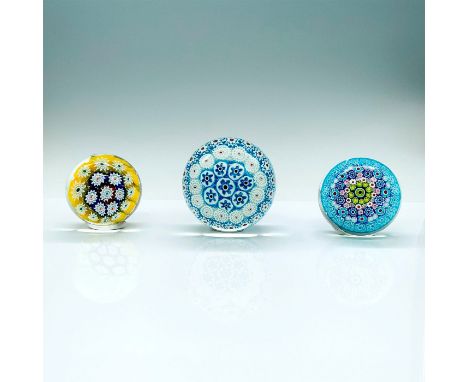 A set of three paperweights that are decorated with abstract floral patterns. One is round clear paperweight with blue and wh