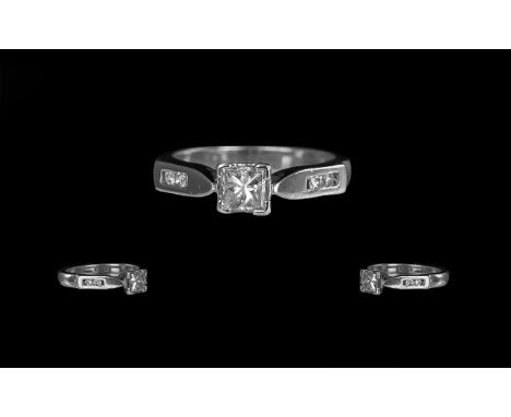 A Platinum Diamond Engagement Ring, set with a central princess cut diamond, four round cut diamond set shoulders.  Central s