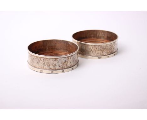A pair of 21st Century sterling silver wine coasters, with bark effect decoration and turned wooden bases, London 2003/4, 12.