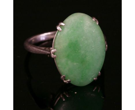 A single stone jade ring,with an oval cabochon jade, double claw set to a shallow collet, with chenier shoulders to a plain s