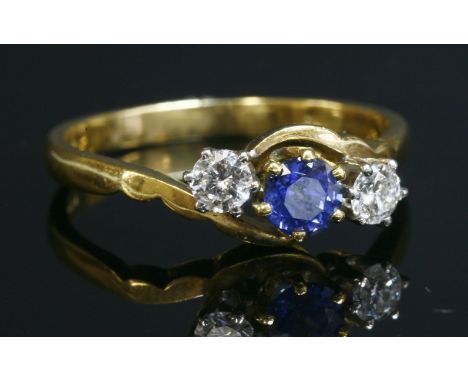 An 18ct gold three stone sapphire and diamond crossover ring,with a central circular mixed cut sapphire, with a stated weight