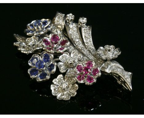 A ruby, sapphire and diamond spray brooch, c.1950,with flower cluster heads of rubies, sapphires and diamonds.  Scrolling ree