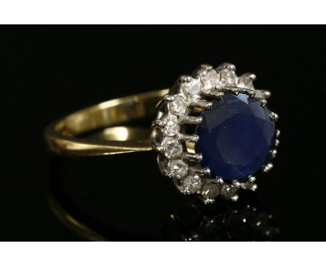 An 18ct gold sapphire and diamond circular cluster ring,with a mixed cut sapphire, surrounded by eight cut diamonds.  All cla