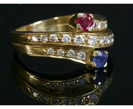 A sapphire, ruby and diamond crossover ring,with a circular mixed cut sapphire and ruby, each four claw set in a plain collet