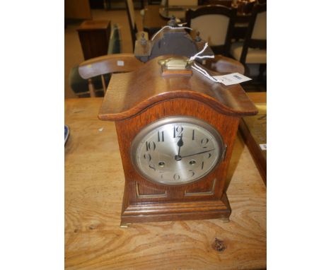 A Victorian mantel clock, with circular silver coloured dial in oak arched case, brass handle, raised on brass feet.