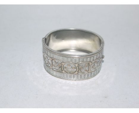 A white metal bangle, the front with engine turned design, rose and yellow metal set floral designs, stamped to clasp "silver