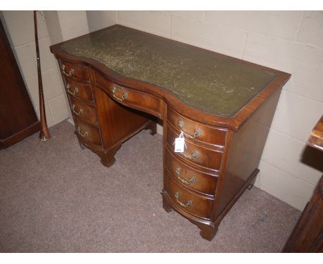 A reproduction mahogany serpentine front kneehole desk, with inset green tooled leather writing surface, fitted a combination