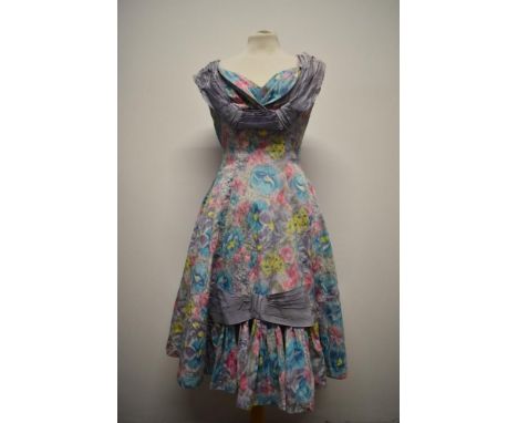 An unusual 1950s day dress, having abstract floral print with contrasting lilac ribbon detailing, pleated sections to front a