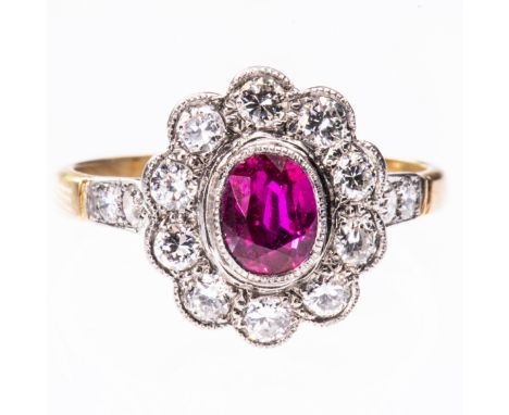 A BURMESE RUBY AND DIAMOND CLUSTER RING, the oval cut Burmese ruby set within a scalloped edge surround of ten brilliant cut 