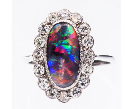 A PLATINUM, BLACK OPAL AND DIAMOND RING, the oval cut opal set within a scalloped mount of brilliant cut diamond highlights b