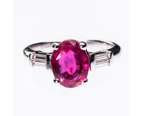 AN 18CT WHITE GOLD RUBY AND DIAMOND RING, the oval cut ruby set between a single baguette cut diamond highlight to each shoul