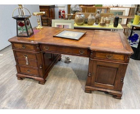 A mahogany twelve drawer, two cupboard door partners desk with shaped top and leather insert, column detailing on bracket fee