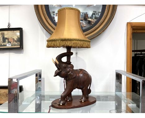 An African carved hardwood elephant form table lamp with tasselled shade, 34.5cm tall (without shade)