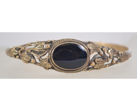 A vintage yellow metal cuff bangle with onyx set cabochon and leaf designed shoulders. Measures 7cms at widest point.