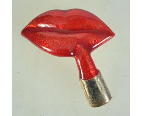 A 1980s goldtone metal and enamel brooch in the form of lips and lipstick having rollover catch. Measures 5.5cms