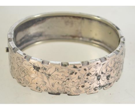 A Victorian silver hinged bangle half engraved with swirling leaf design and castellated edge with box clasp. Marked SILVER m