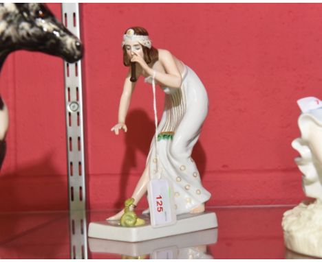 A Rosenthal figure of a female snake charmer, circa 1920, scantily clad and bending down playing a pipe over a small green co