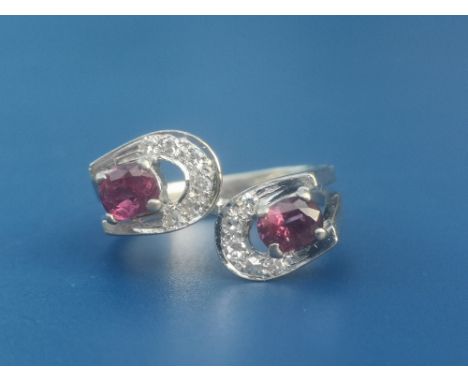 A modern ruby &amp; diamond set 18ct white gold double horseshoe ring in crossover style, a claw set oval cut ruby to the cen