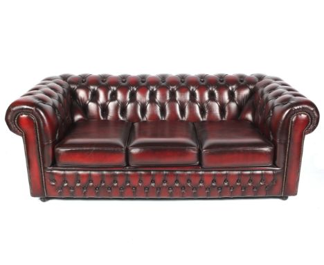 A modern Chesterfield three person settee. By Saxon upholstered in Burgundy leather with outswept scrolled arms  raised on ca