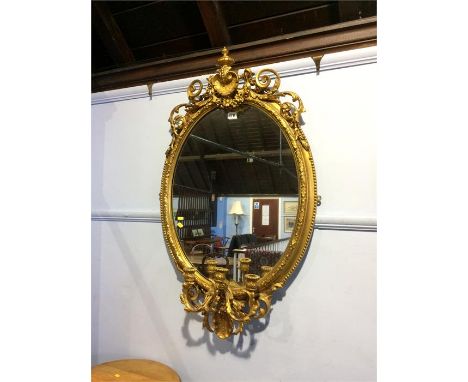 An ornate gilt oval mirror with three branch candelabra