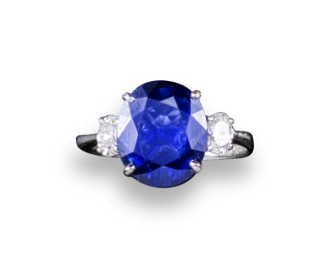 A sapphire and diamond three-stone ring, the oval-shaped sapphire is set with an oval-shaped diamond to each shoulder in whit