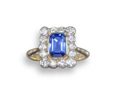 A sapphire and diamond cluster ring, the emerald-cut sapphire set within a surround of graduated circular-cut diamonds in yel