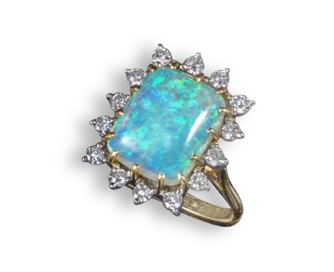 An opal and diamond cluster ring, the rectangular-shaped opal set within a surround of fourteen circular-cut diamonds in yell