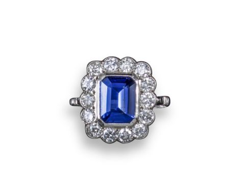 A tanzanite and diamond cluster ring, the emerald-cut tanzanite is rubover-set within a surround of circular-cut diamonds in 