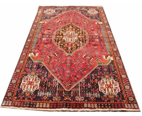 A Caucasian hand woven wool carpet, worked with an all over foliate design, with a central medallion against a red ground, 25