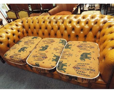 A tan leather button-back three-seater Chesterfield with tapestry style cushions