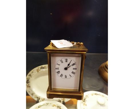 A brass carriage time piece with enamel dial, Roman numerals and bevel glass viewing panels