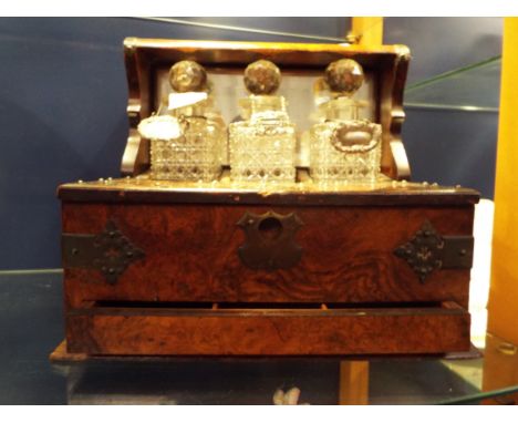 A Victorian burr walnut and brass bound tantalus with games drawer including three hobnail cut decanters, counters, two bridg
