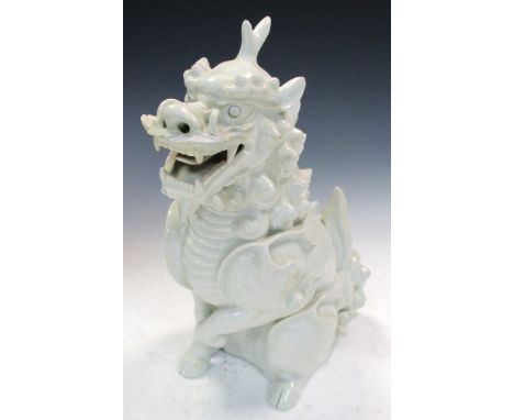 A 19th century white glazed figure of a seated qilin, its mouth opened in a mischievous grin, one front hoof raised, its body